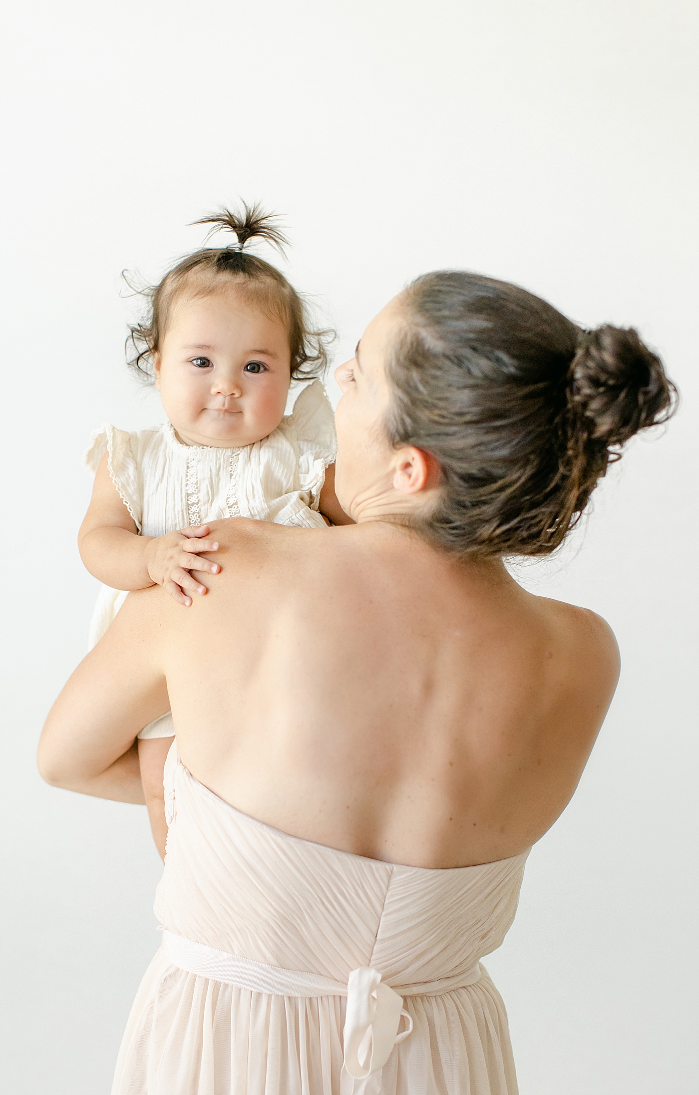 Baby girl held by mom looking over her shoulder | Image by Chrissy Winchester Photography