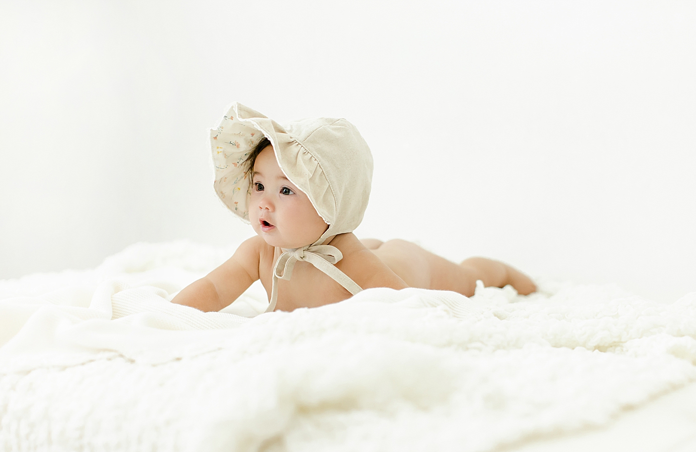 Baby girl in a bonnet laying on her belly | Image by Chrissy Winchester Photography