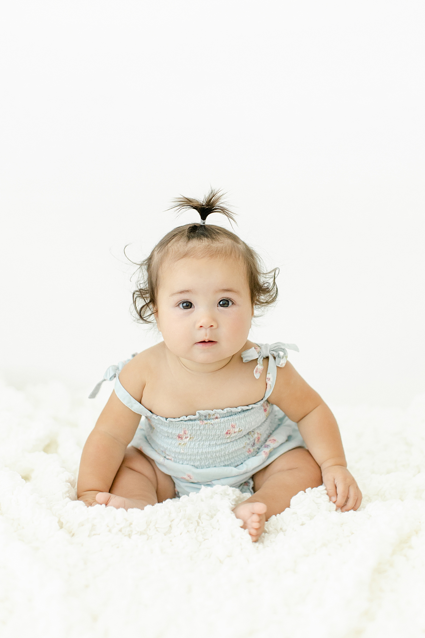 Baby girl in tiny ponytails in a blue jumper during her Six Month Studio Session | Image by Chrissy Winchester Photography