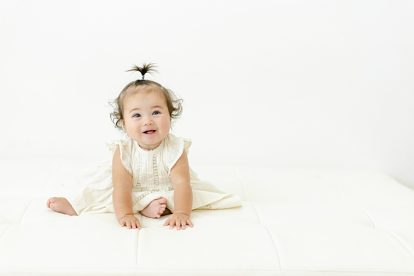 Baby girl practicing her sitting in a cream dress | Image by Chrissy Winchester Photography