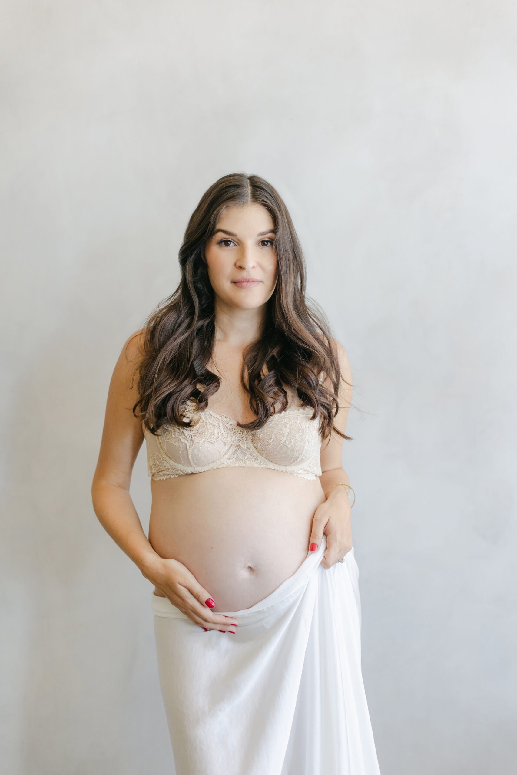 expecting mom with long brown hair thoughtfully holding belly while looking at camera