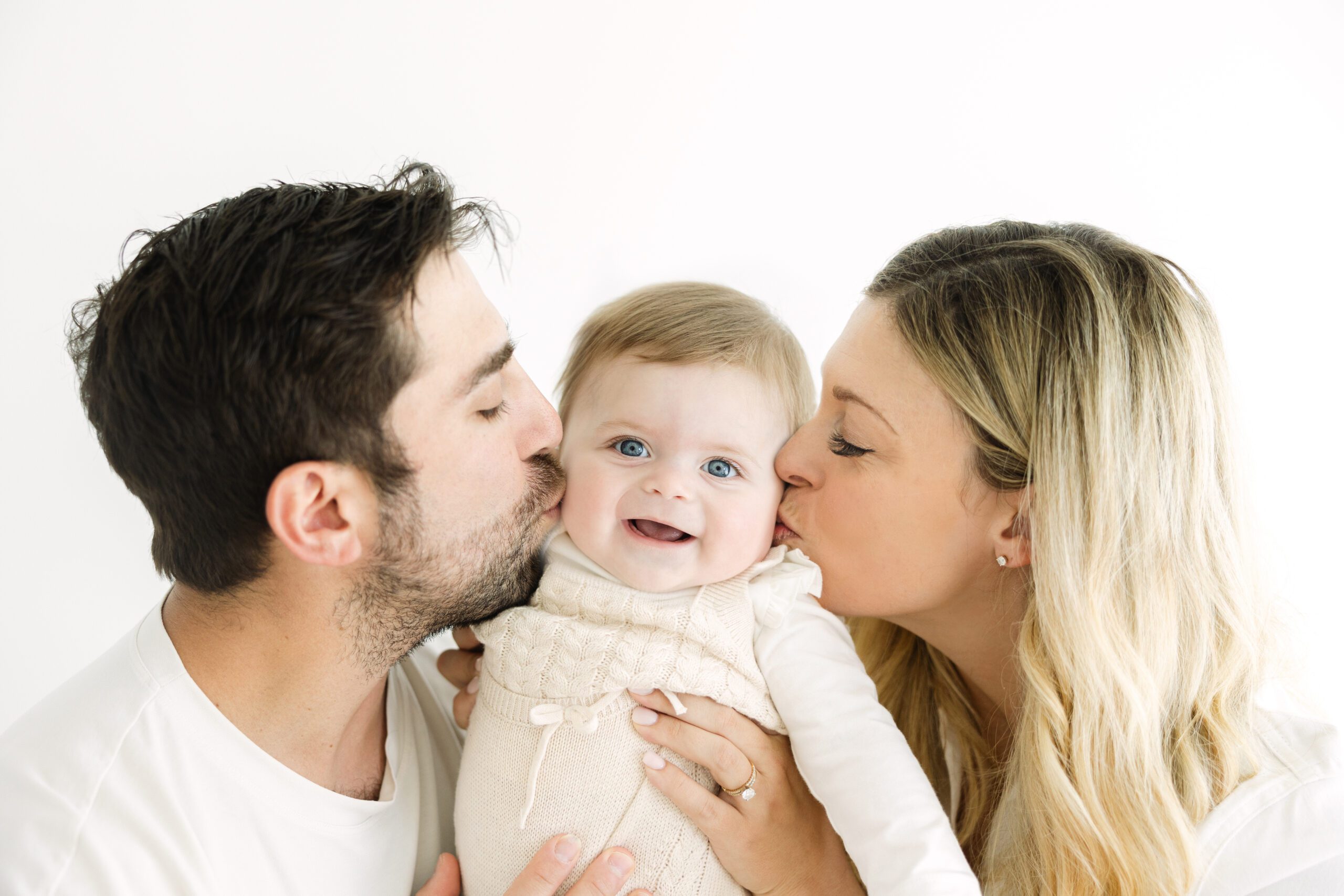 Mom and Dad kissing their baby on the cheek | Image by Chrissy Winchester