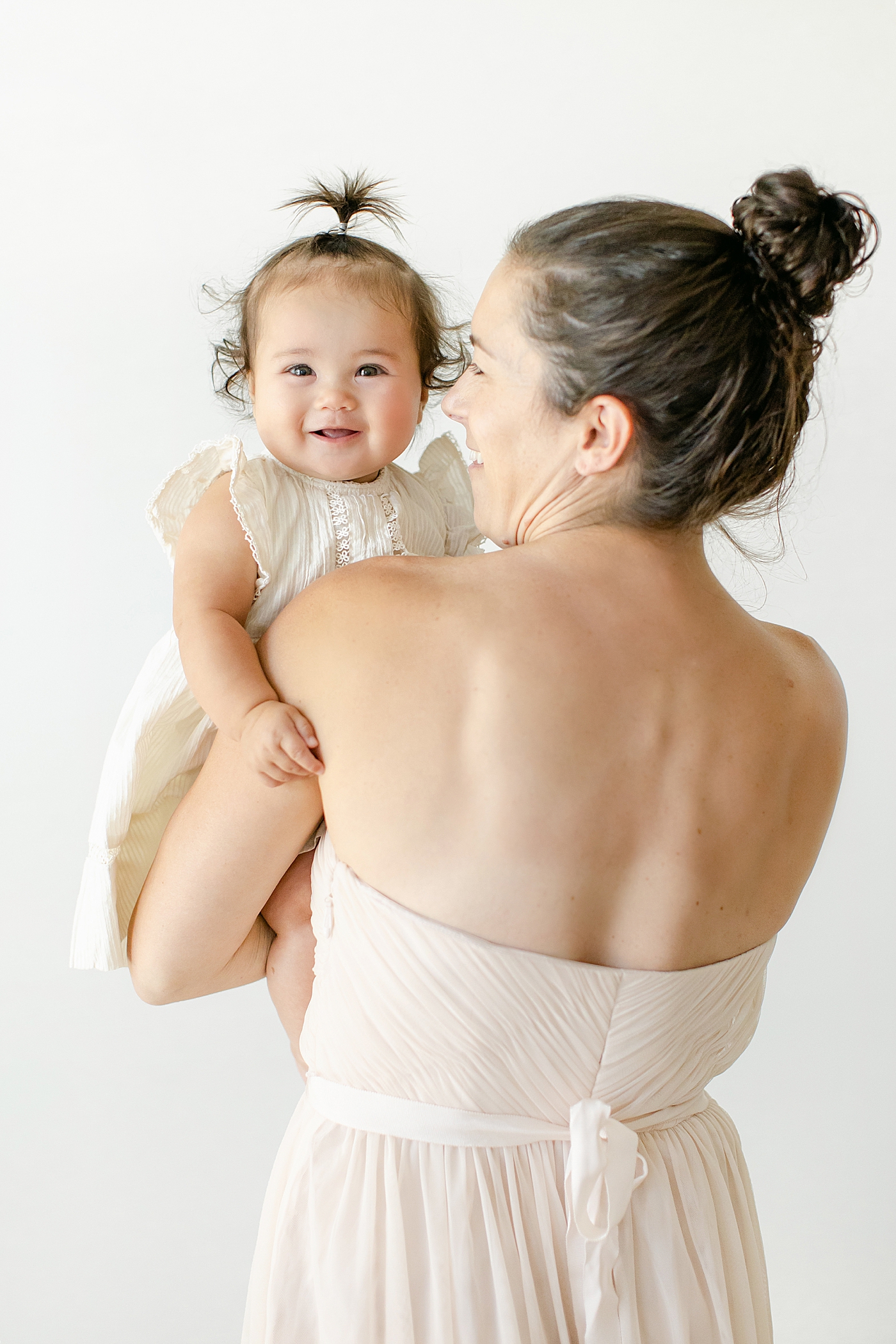 Baby girl in a white dress held by mom in sleeveless pink dress | Image by Chrissy Winchester Photography