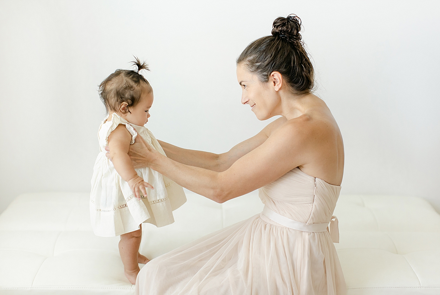 Mom and baby girl sitting on a white bed | Image by Chrissy Winchester Photography