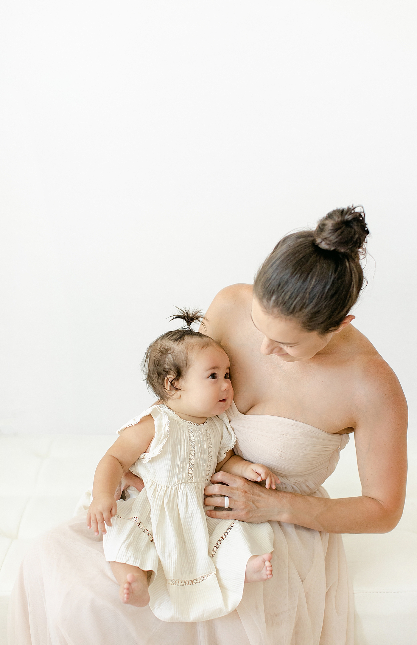 Mom holding her baby girl while they wear matching cream dresses during her Six Month Studio Session | Image by Chrissy Winchester Photography