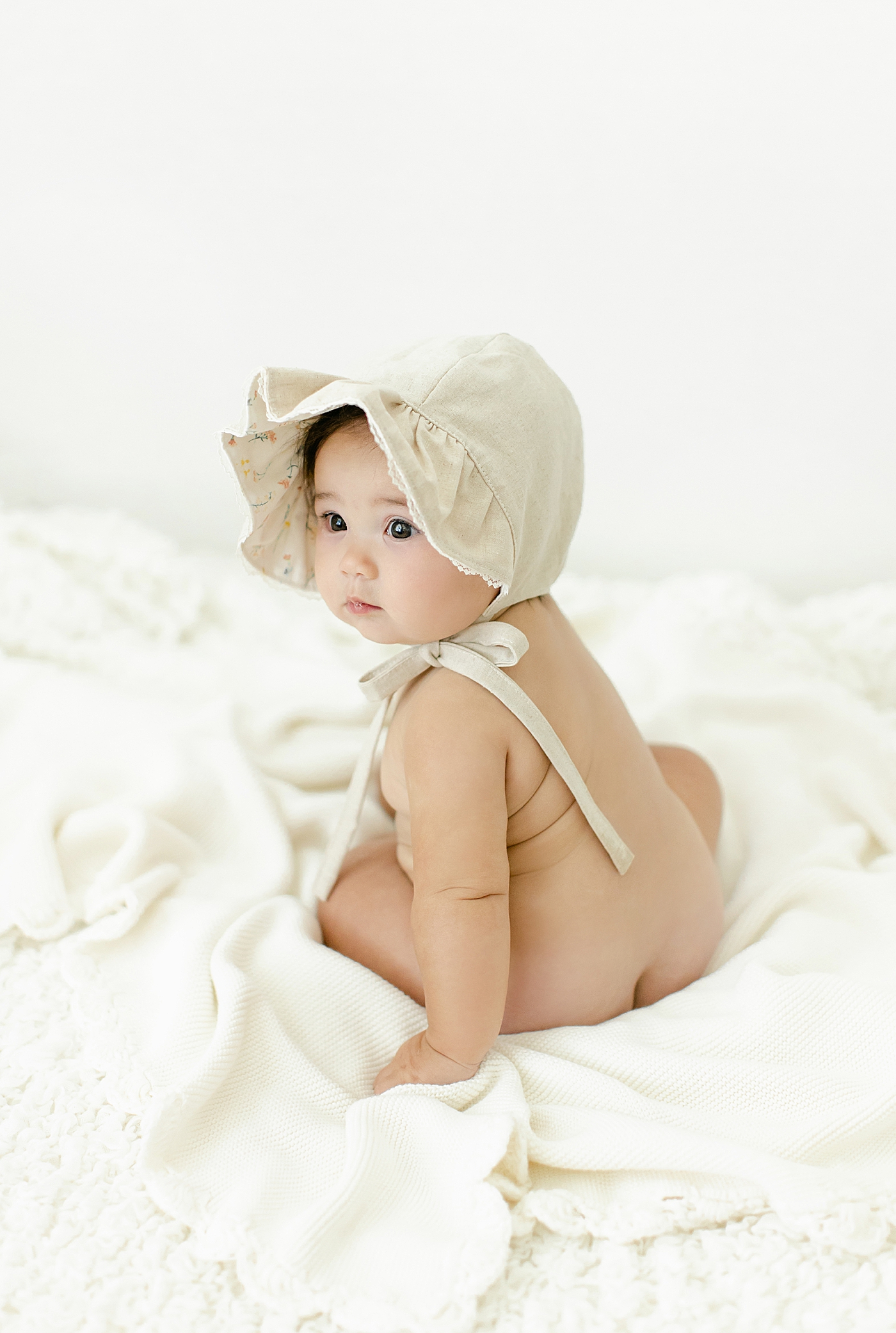 Sitting baby girl wearing a bonnet during her Six Month Studio Session | Image by Chrissy Winchester Photography