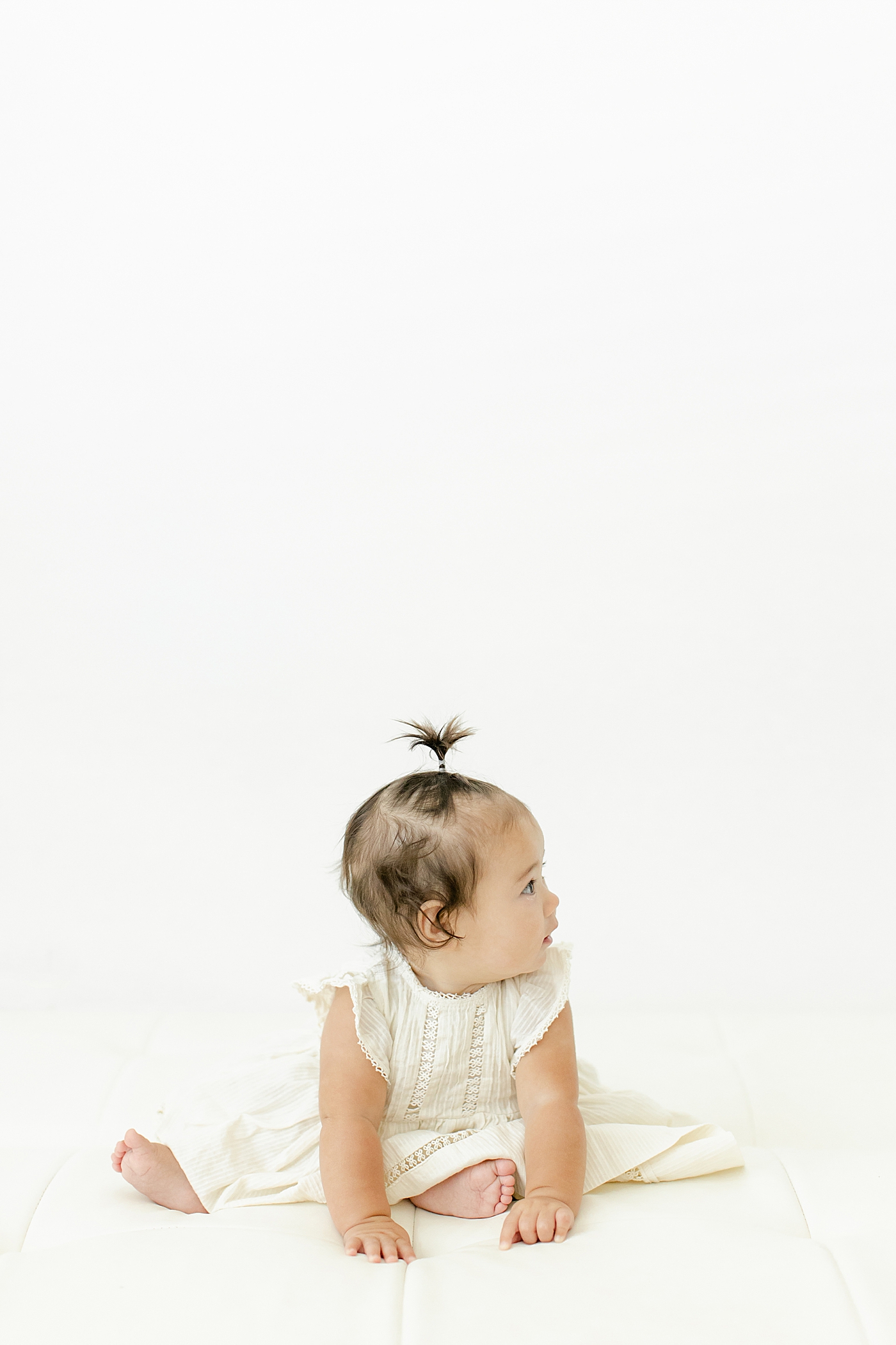 Baby girl sitting up wearing a cream dress during her Six Month Studio Session | Image by Chrissy Winchester Photography