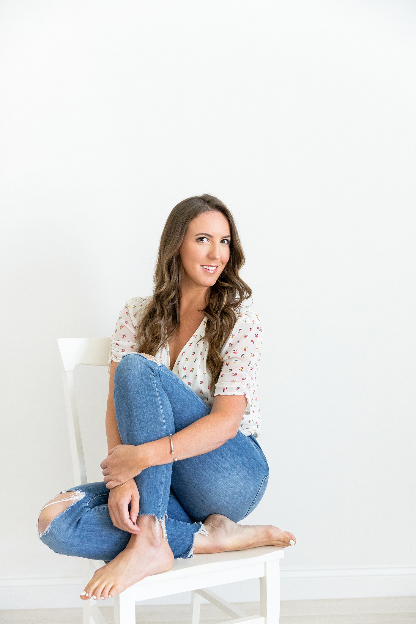 Woman in a white top and jeans sitting in a white chair | Image by Chrissy Winchester Photography