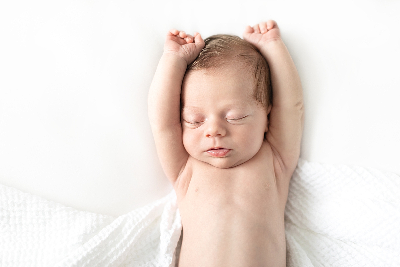 Newborn baby stretching wrapped in a white swaddle | Imaged by Chrissy Winchester