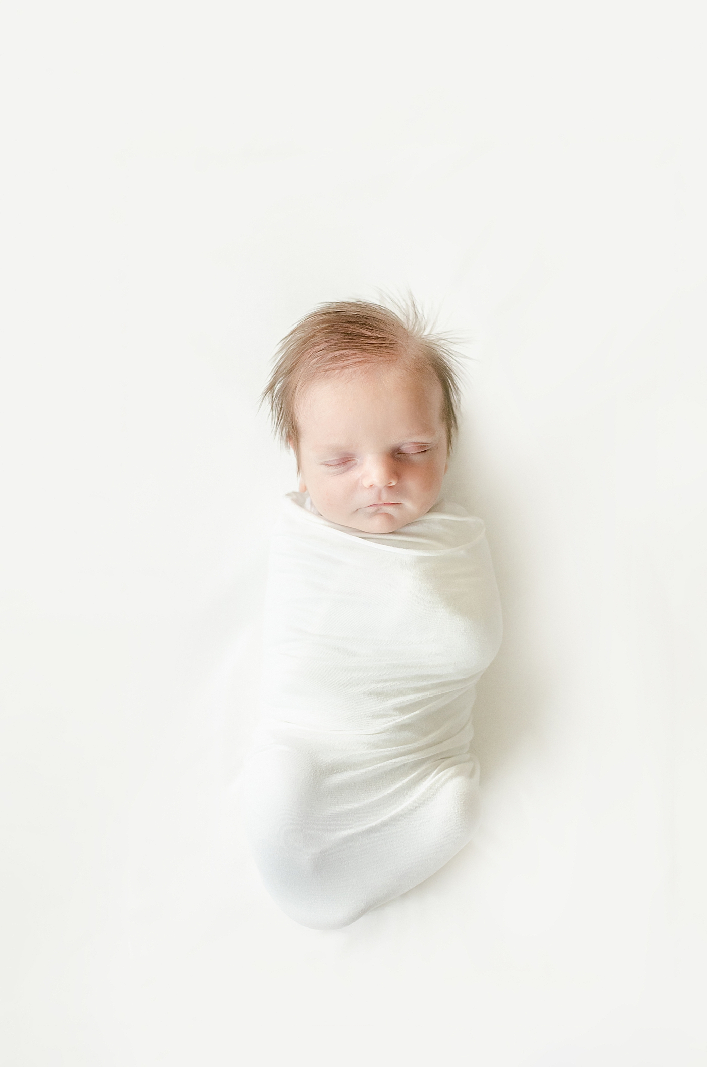Sleeping newborn baby wrapped in a white swaddle | Image by Chrissy Winchester Photography